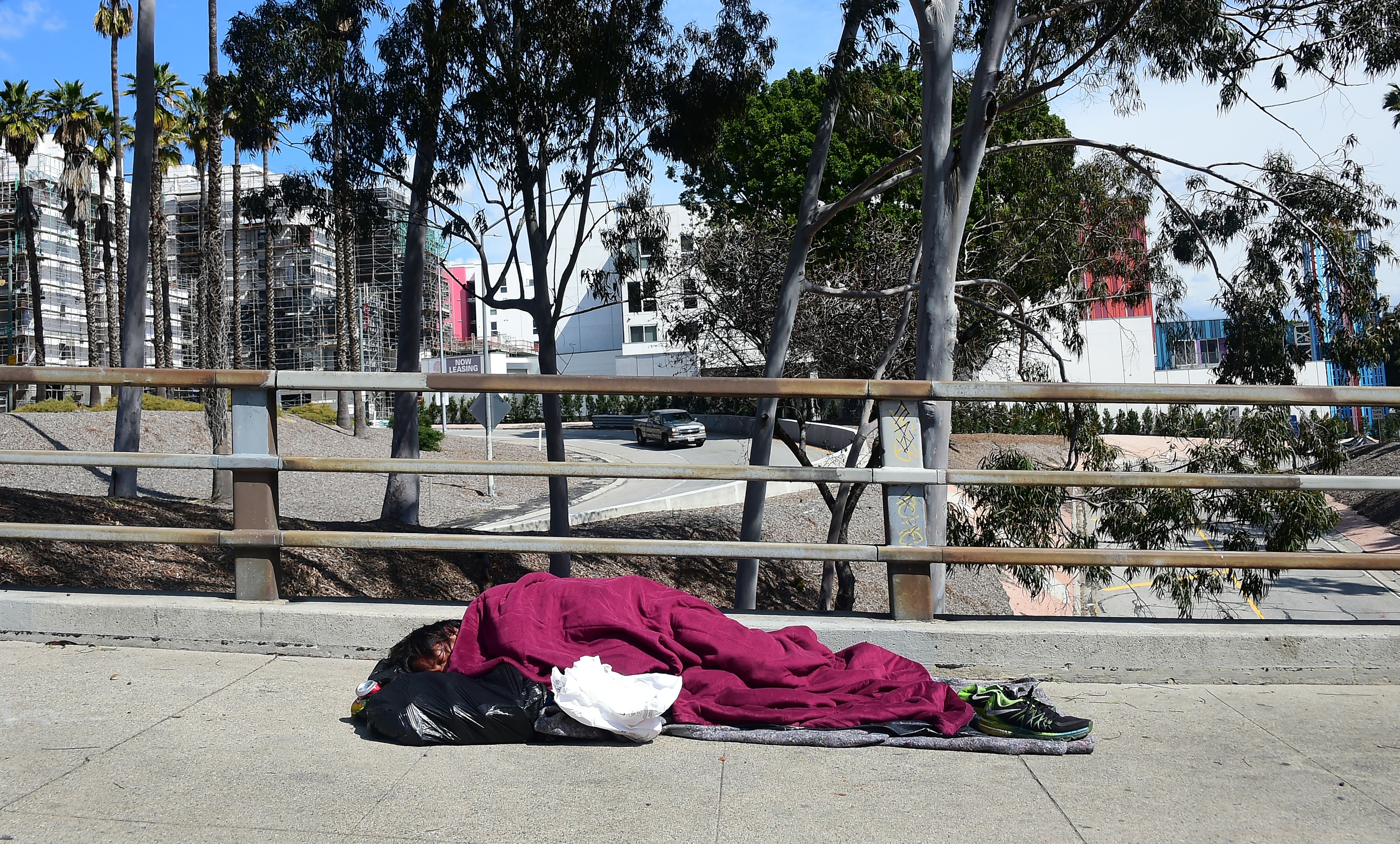 A homeless man sleeps on a sidewalk in Los Angeles on March 10, 2019. (Credit: Frederic J. Brown / AFP / Getty Images)