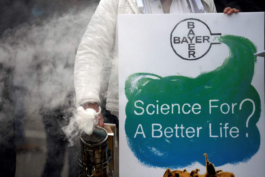 A protestor stands with a bee smoker and a placard reading "Science for a better life?" during a demonstration outside the World Conference centre where the annual general meeting of German chemicals giant Bayer takes place on April 26, 2019 in Bonn, western Germany. (Credit: INA FASSBENDER/AFP/Getty Images)