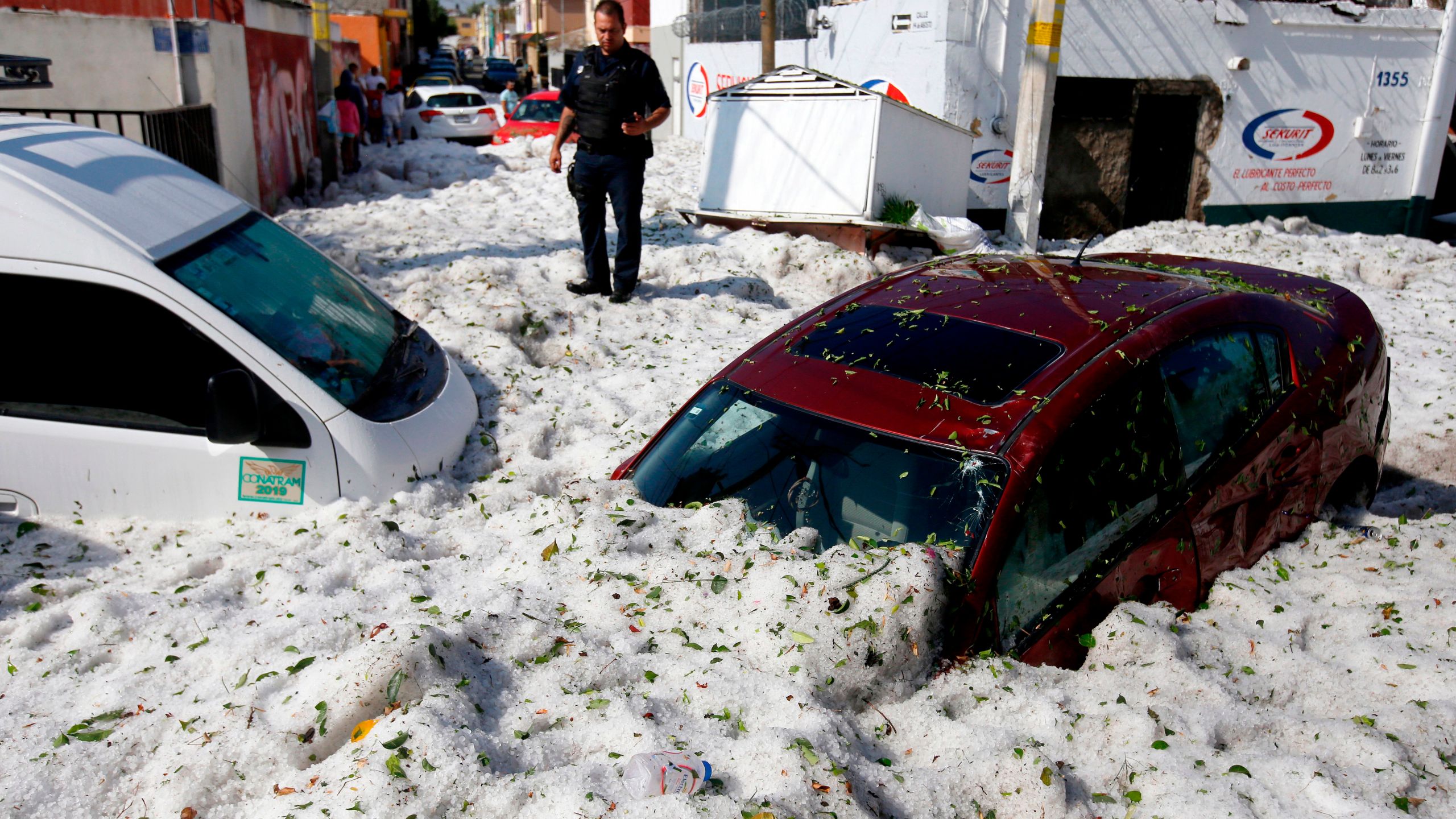 A police officer stands next to vehicles buried in hail in the eastern area of Guadalajara, Jalisco state, Mexico, on June 30, 2019. (Credit: ULISES RUIZ/AFP/Getty Images)