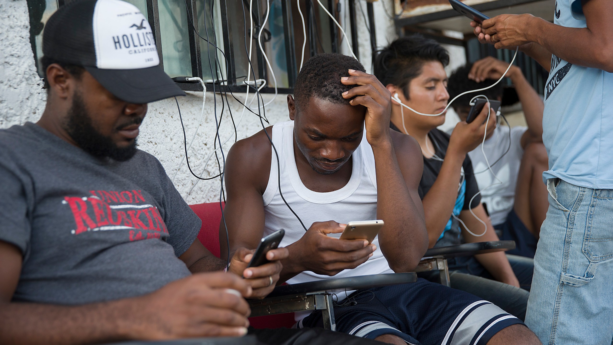 Migrants from Cameroon use their cell phones as they relax at the Albergue Para Migrantes El Buen Samaritano while waiting to have their number on a waiting list that is months long to be called to have an initial interview with a U.S. asylum officer on June 5, 2019, in Ciudad Juarez, Mexico. (Credit: Joe Raedle/Getty Images)