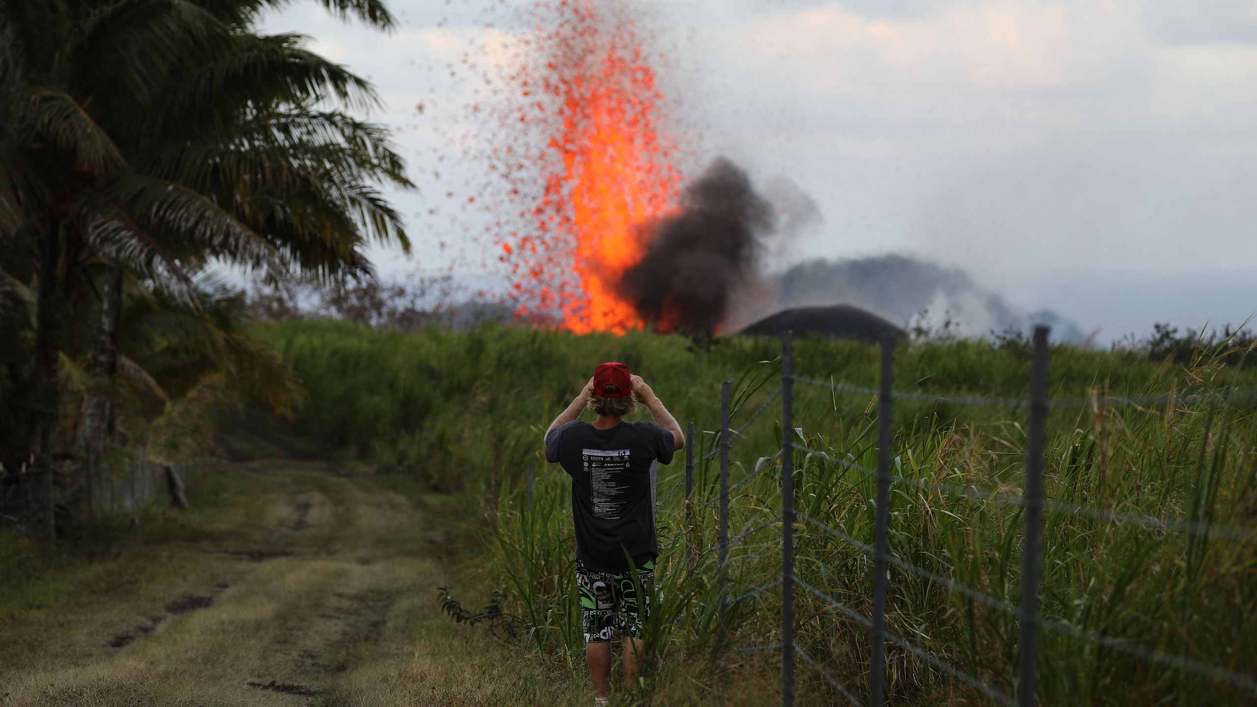 A man takes a photo of a lava fountain from a Kilauea volcano fissure on Hawaii's Big Island on May 18, 2018, in Kapoho, Hawaii. (Credit: Mario Tama/Getty Images)