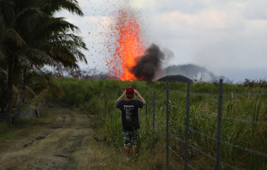 A man takes a photo of a lava fountain from a Kilauea volcano fissure on Hawaii's Big Island on May 18, 2018, in Kapoho, Hawaii. (Credit: Mario Tama/Getty Images)