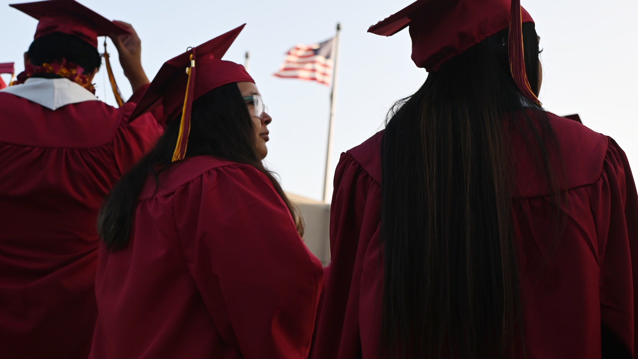 A U.S. flag flies above a building as students earning degrees at Pasadena City College participate in the graduation ceremony, June 14, 2019, in Pasadena, Calif. With 45 million borrowers owing $1.5 trillion, the student debt crisis in the U.S. has exploded in recent years and has become a key electoral issue in the run-up to the 2020 presidential elections. (Credit: ROBYN BECK/AFP/Getty Images)