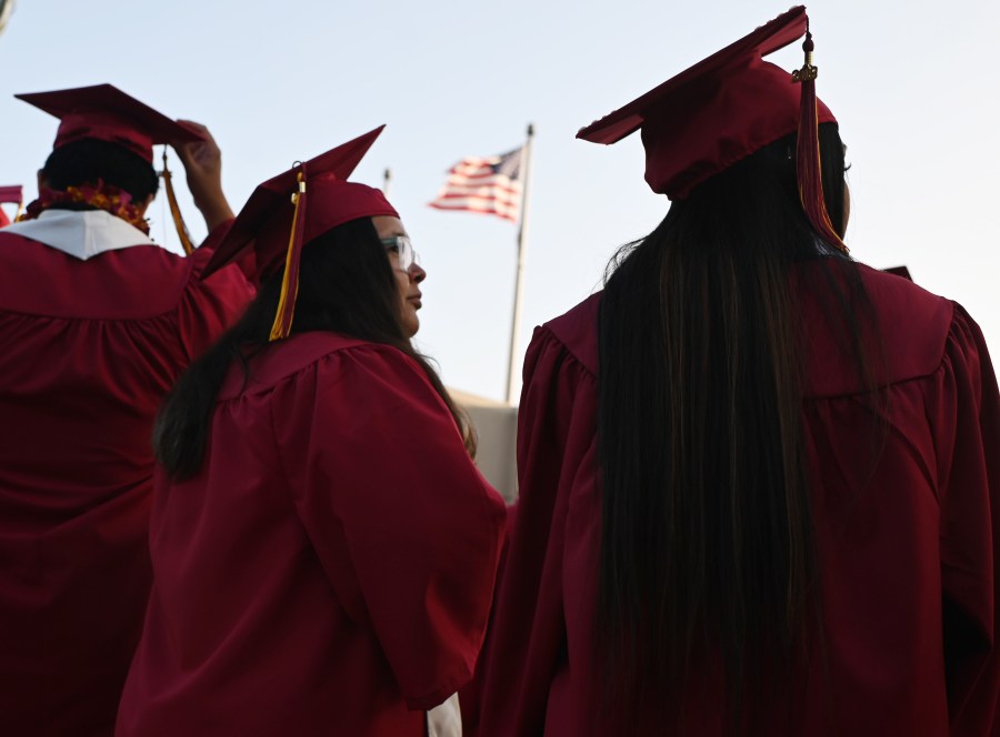 A U.S. flag flies above a building as students earning degrees at Pasadena City College participate in the graduation ceremony, June 14, 2019, in Pasadena, Calif. With 45 million borrowers owing $1.5 trillion, the student debt crisis in the U.S. has exploded in recent years and has become a key electoral issue in the run-up to the 2020 presidential elections. (Credit: ROBYN BECK/AFP/Getty Images)