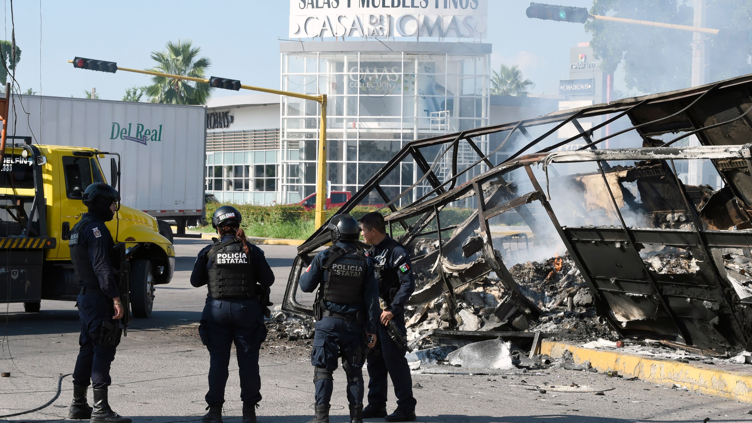 Policemen stand next to a burnt vehicle after heavily armed gunmen waged an all-out battle against Mexican security forces in Culiacan, Sinaloa state, Mexico, on Oct. 18, 2019. (Credit: ALFREDO ESTRELLA / AFP/Getty Images)