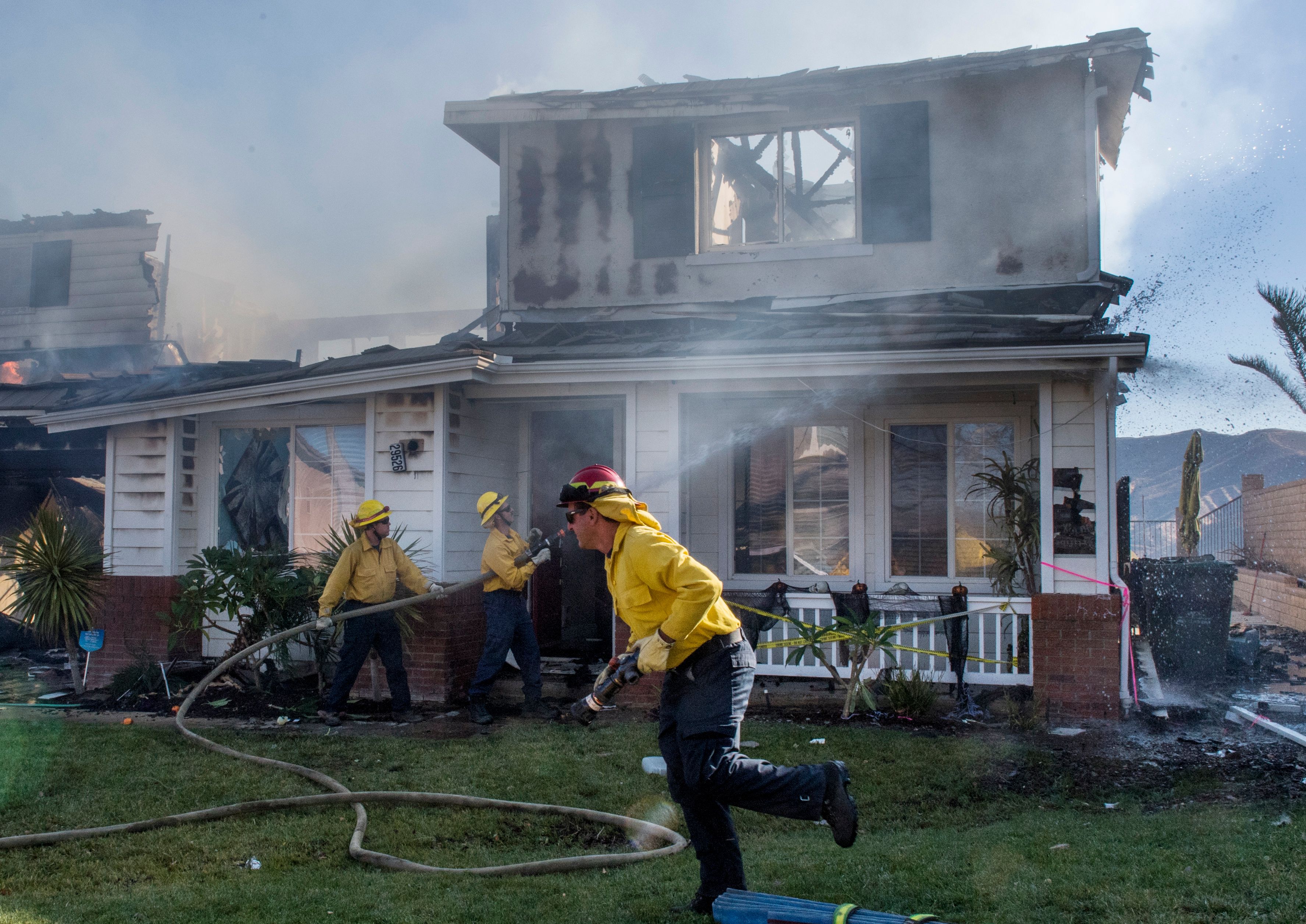 Firefighters hose down a burning house during the Tick Fire in Agua Dulce near Santa Clarita, California on Oct. 25, 2019. (Credit: MARK RALSTON/AFP via Getty Images)