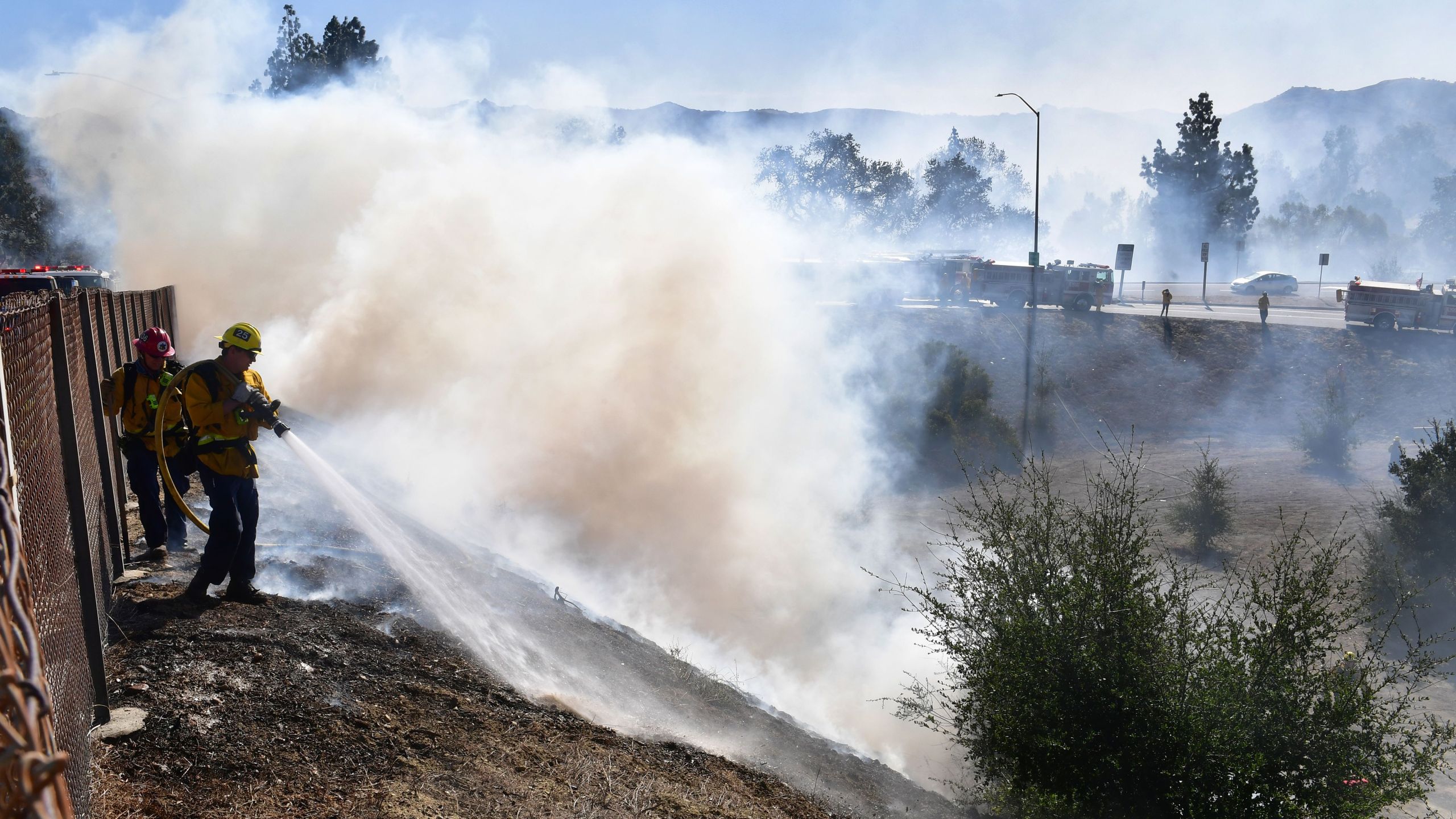 A firefighter sprays water on charred hillside near homes and the 118 Freeway in Simi Valley on Oct. 30, 2019. (Credit: Frederic J. Brown / AFP / Getty Images)