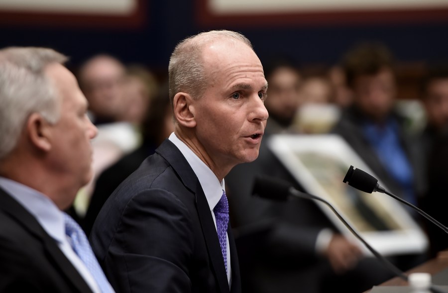 Family members of those who died aboard Ethiopian Airlines Flight 302 hold photographs of their loved ones as Dennis Muilenburg, right, testifies at a hearing in front of congressional lawmakers on Capitol Hill in Washington, D.C. on Oct. 30, 2019. (Credit: OLIVIER DOULIERY/AFP via Getty Images)