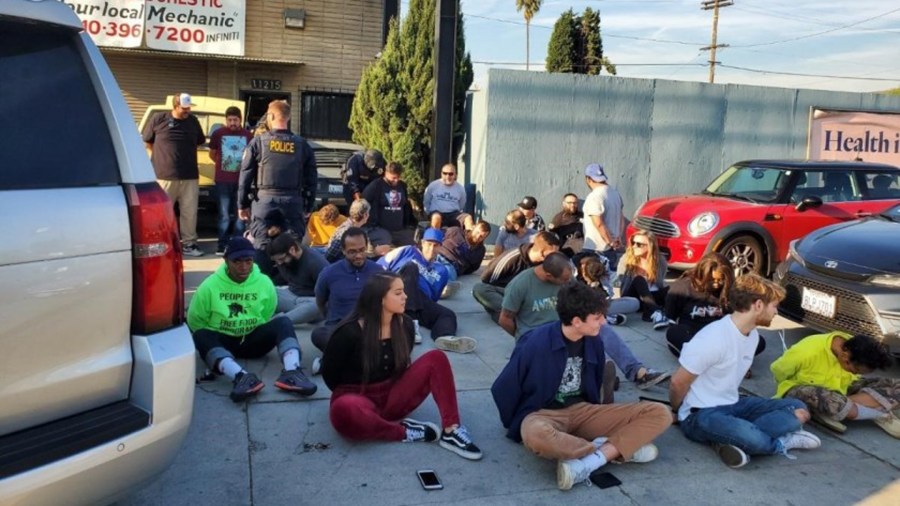 Subjects sit on the ground with their hands zip-tied following an unlicensed dispensary raid in Palms on Dec. 12, 2019. (Credit: California Bureau of Cannabis Control via Los Angeles Times)