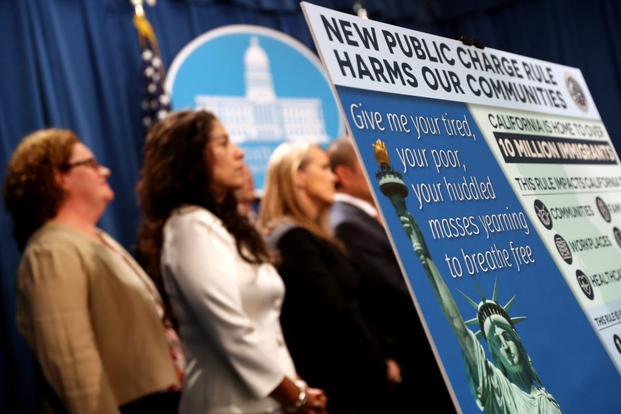 A sign is displayed during a news conference on Aug. 16, 2019 in Sacramento announcing a lawsuit against the Trump administration over the legality of a "public charge" rule that would make it difficult for immigrants on public assistance to obtain green cards. (Credit: Justin Sullivan/Getty Images)