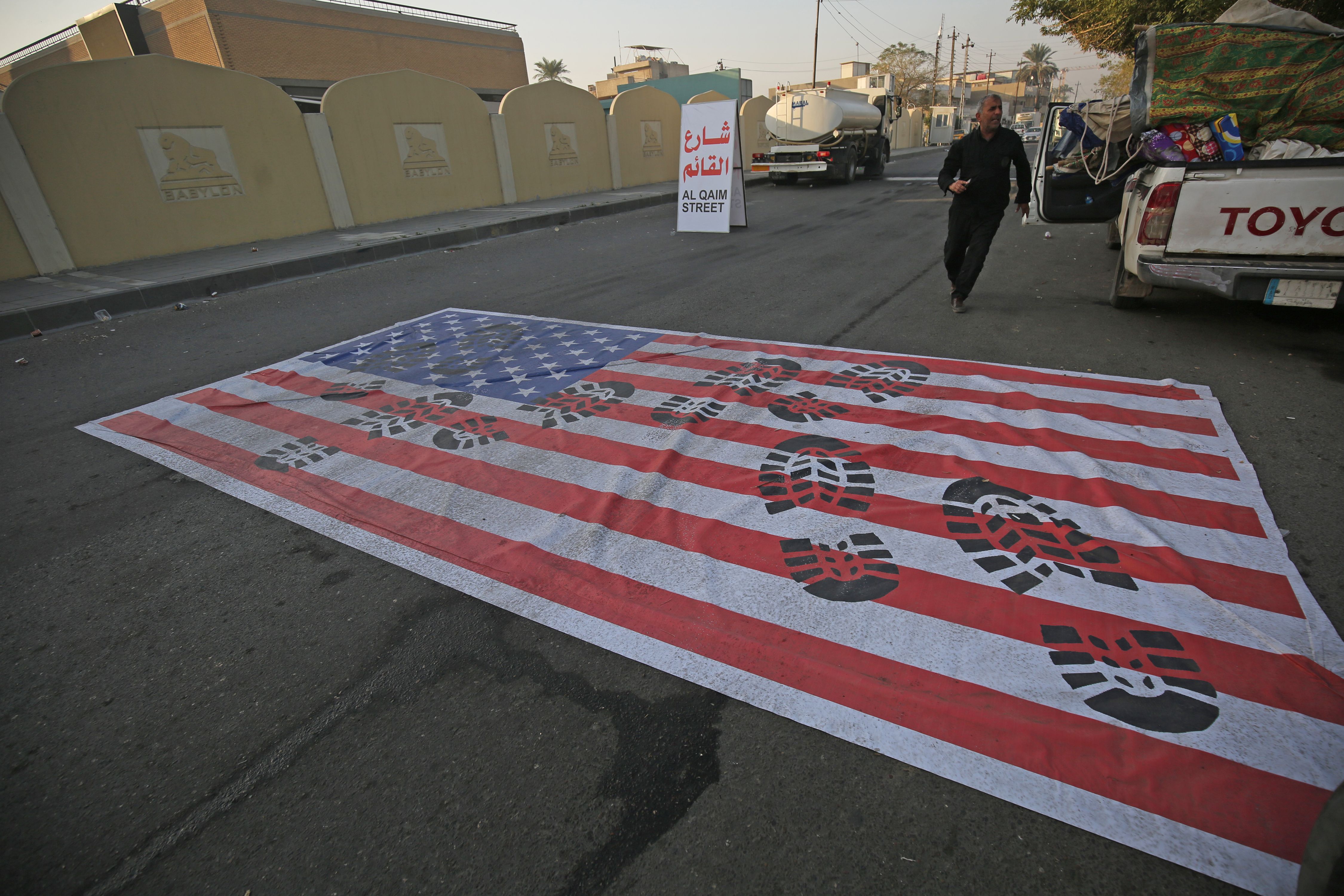 A mock US flag is laid on the ground for cars to drive on in the Iraqi capital Baghdad on January 3, 2020, following news of the killing of Iranian Revolutionary Guards top commander Qasem Soleimani in a US strike on his convoy at Baghdad international airport. (Credit: AHMAD AL-RUBAYE/AFP via Getty Images)