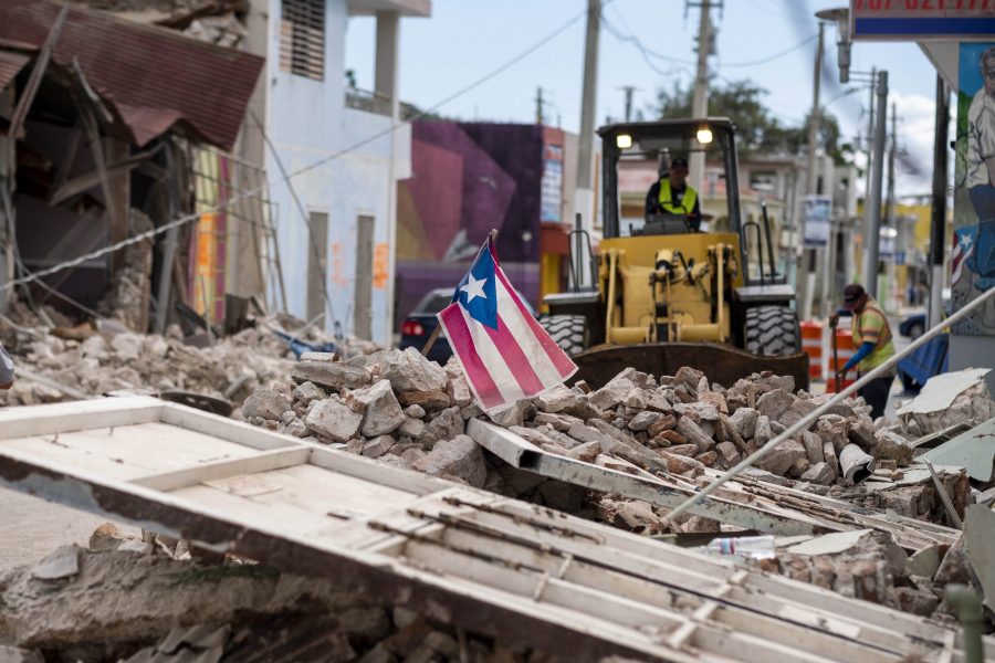 A Puerto Rican flag waves on top of a pile of rubble as debris is removed from a main road in Guanica, Puerto Rico on Jan. 8, 2020. (Credit: RICARDO ARDUENGO/AFP via Getty Images)