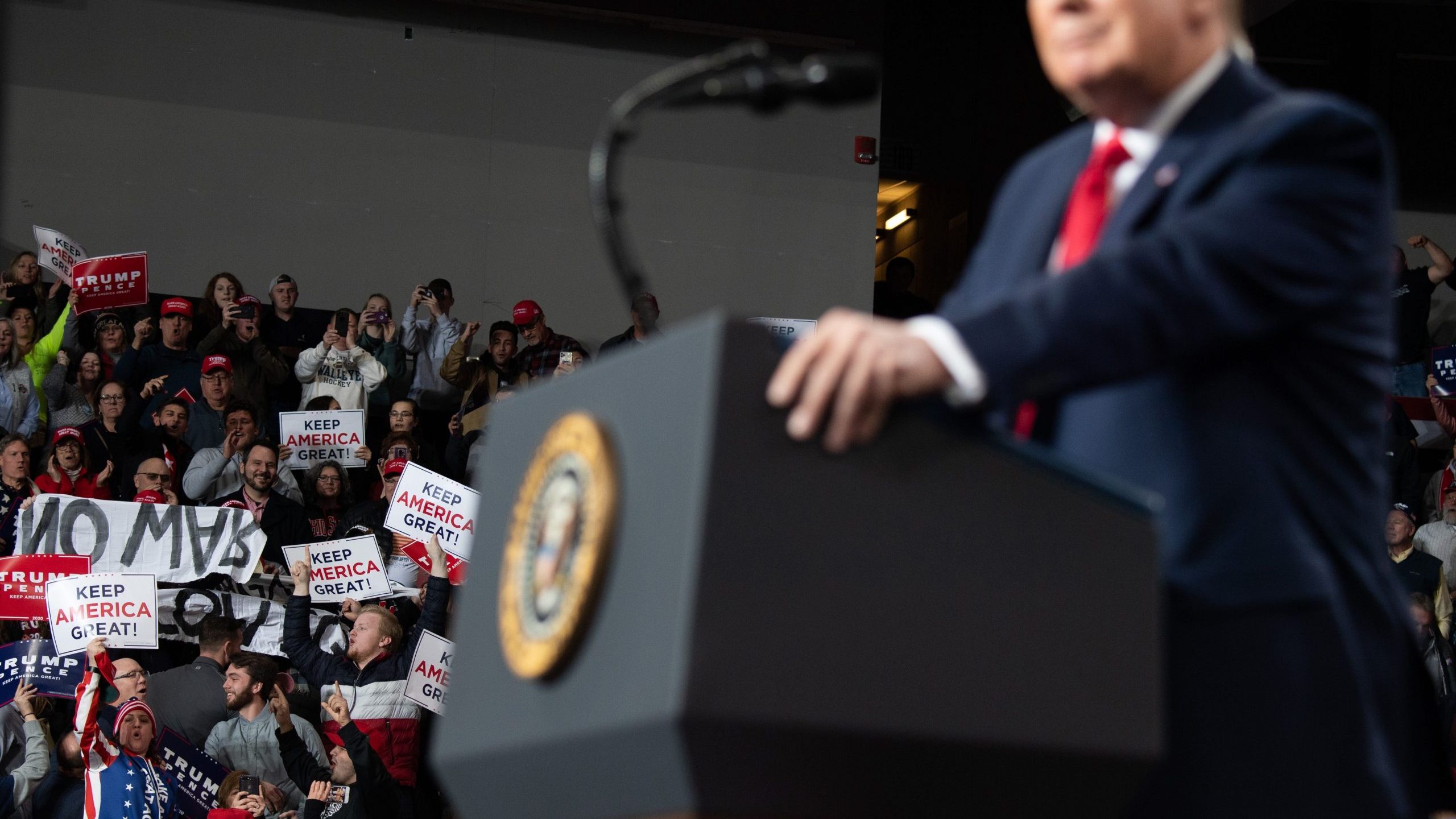 Protesters hold signs as U.S. President Donald Trump holds a "Keep America Great" campaign rally at Huntington Center in Toledo, Ohio, on Jan. 9, 2020. (Credit: Saul Loeb / AFP via Getty Images)