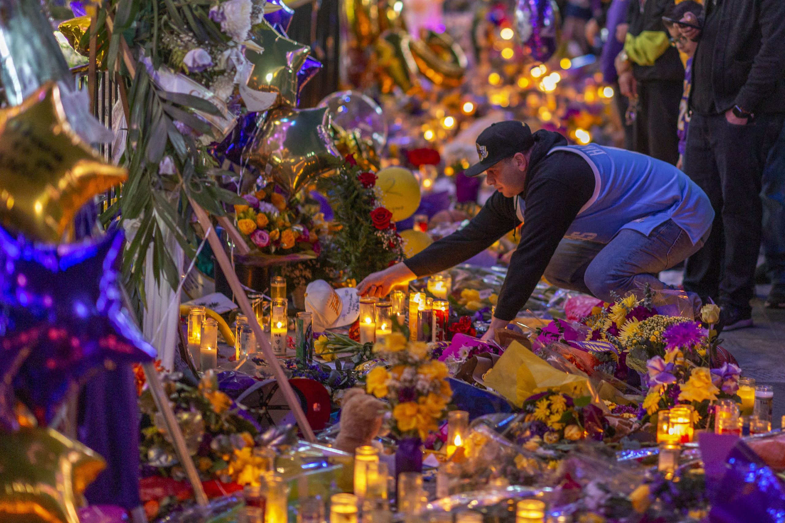 A man places a hat at a makeshift memorial near Staples Center in remembrance of former NBA great Kobe Bryant who, along with his 13-year-old daughter Gianna, died January 26 in a helicopter crash, on January 28, 2020 in Los Angeles, California. (Credit: David McNew/Getty Images)