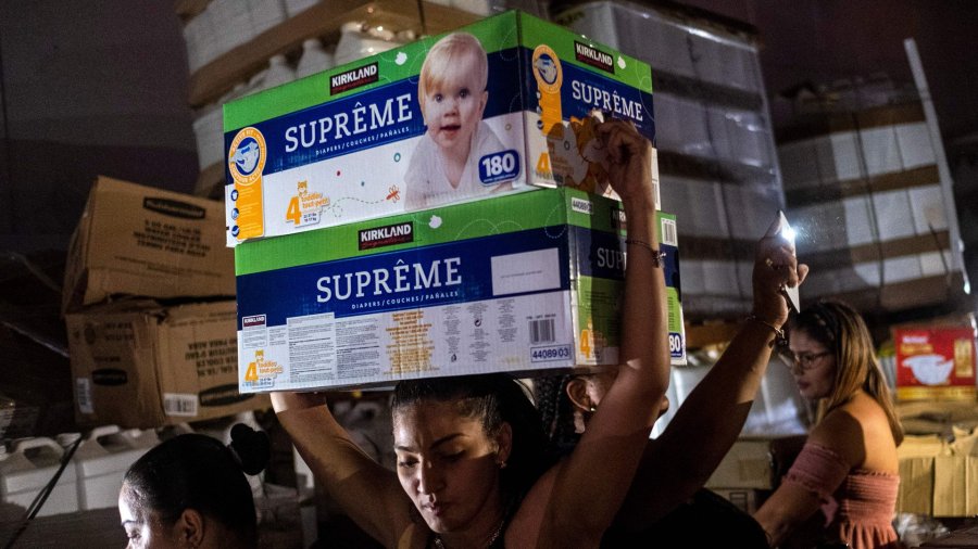 A woman carries boxes of baby diapers from warehouse filled with supplies, including thousands of cases of water, believed to have been from when Hurricane Maria struck the island in 2017 in Ponce, Puerto Rico on January 18, 2020, after a powerful earthquake hit the island. (Credit: Ricardo Arduengo/AFP’Getty Images)