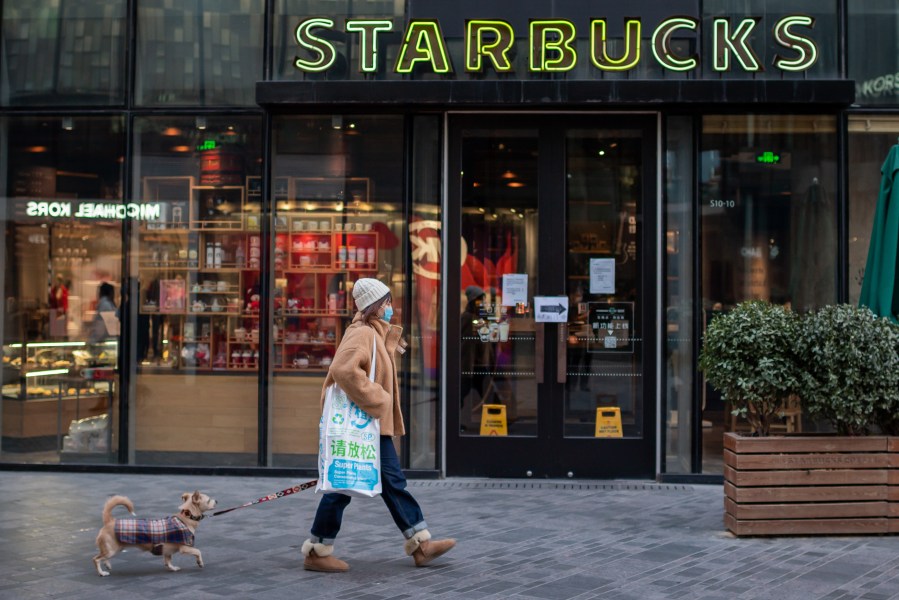 A woman, wearing a protective facemask, walks past a Starbucks coffee shop with her dog in Beijing on Jan. 30, 2020. (NICOLAS ASFOURI/AFP via Getty Images)