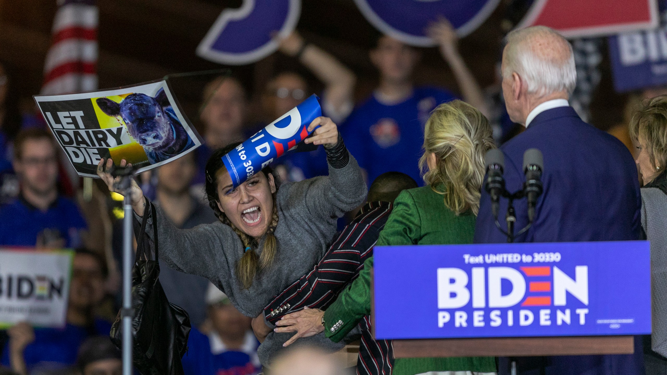 A woman charges the stage while holding a sign that reads "Let Dairy Die" as Democratic presidential candidate former Vice President Joe Biden speaks at a Super Tuesday event at Baldwin Hills Recreation Center on March 3, 2020, in Los Angeles. (David McNew/Getty Images)