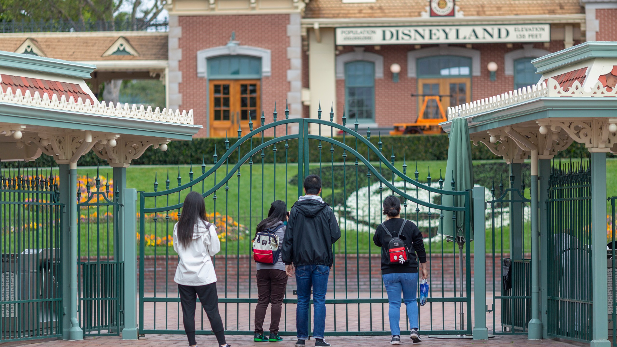 People stand outside the gates of Disneyland in Anaheim on the first day of the park's closure due to coronavirus, March 14, 2020. (Credit: David McNew / AFP / Getty Images)