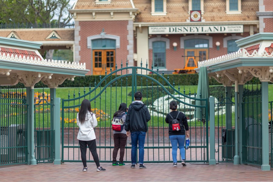 People stand outside the gates of Disneyland in Anaheim on the first day of the park's closure due to coronavirus, March 14, 2020. (Credit: David McNew / AFP / Getty Images)