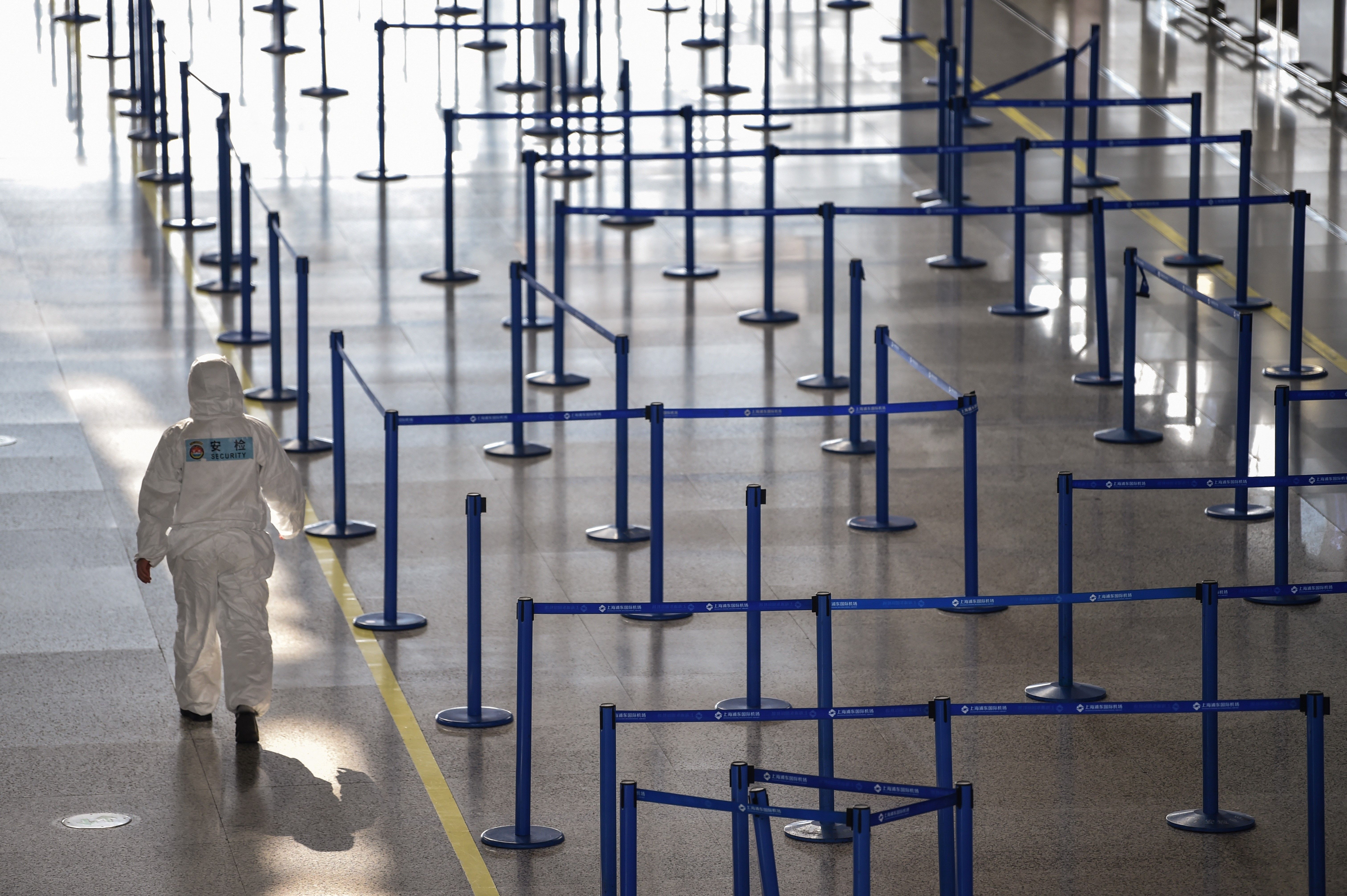 An airport security worker wearing protective gear while walking past check-in counters at Shanghai Pudong International Airport on March 18, 2020. (Hector Retamal/AFP via Getty Images)