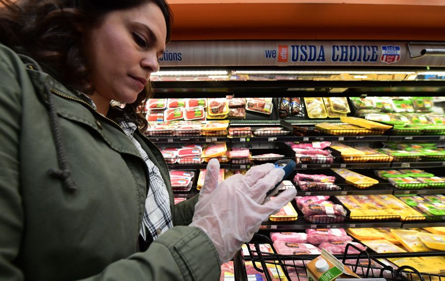 Instacart employee Monica Ortega wears gloves while using her cellphone to check orders while picking up groceries from a supermarket for delivery on March 19, 2020, in North Hollywood. (FREDERIC J. BROWN/AFP via Getty Images)