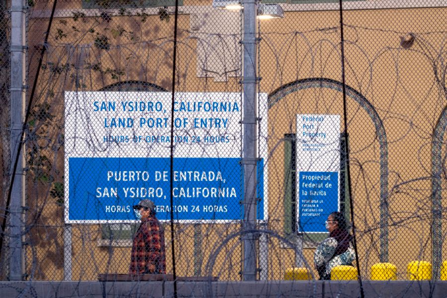 People wear face masks as they walk at San Ysidro port of entry on the Mexico-U.S. border as seen from Tijuana on March 21, 2020. (Guillermo Arias/ AFP / Getty Images)