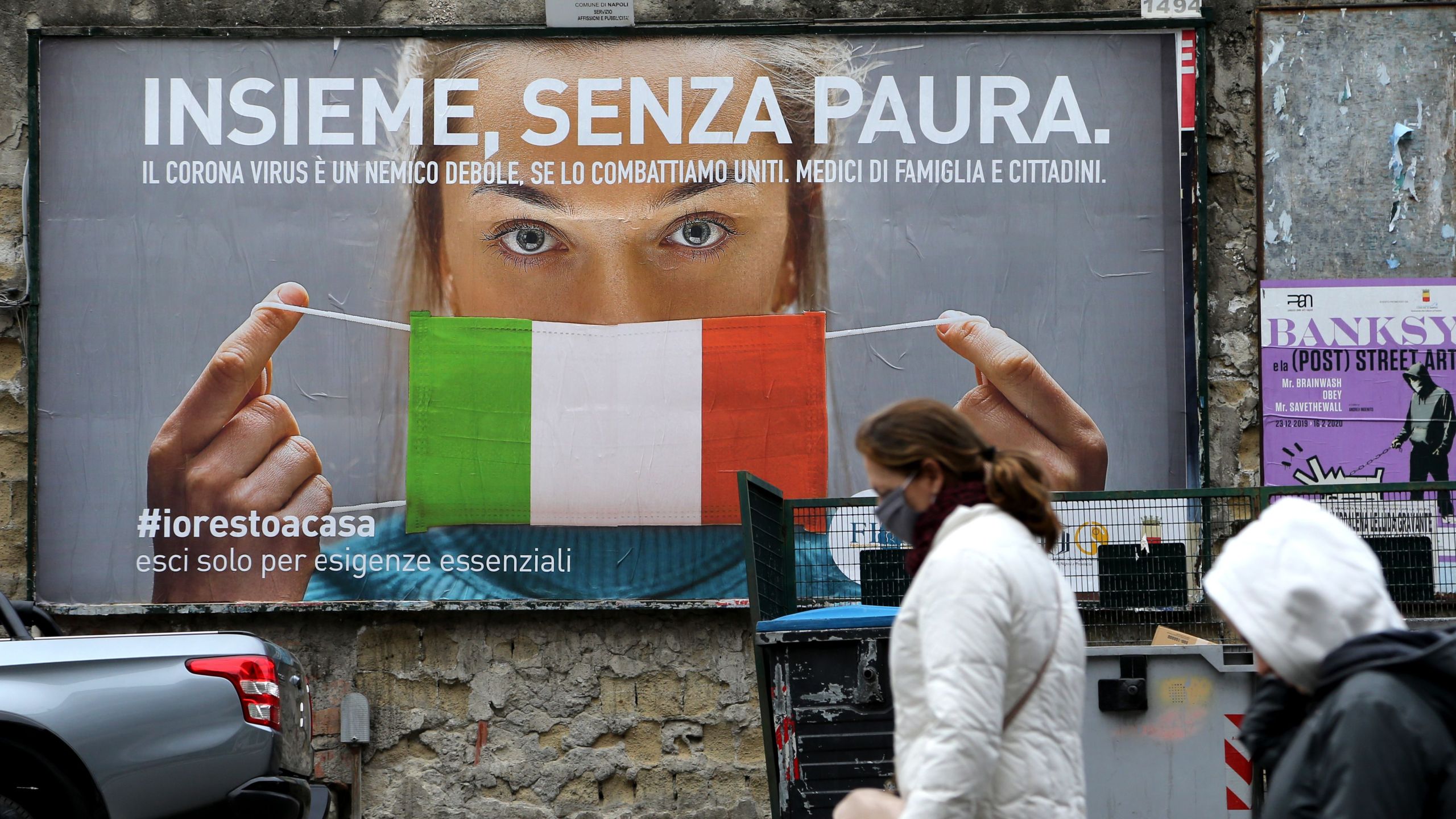 People walk past a huge billboard that shows a woman with a protective mask in the colors of an Italian flag, which reads, "All together, without fear," referring to the government campaign to stay home in the city of Naples, Italy, on March 22, 2020. (CARLO HERMANN/AFP via Getty Images)