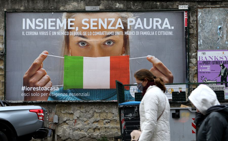 People walk past a huge billboard that shows a woman with a protective mask in the colors of an Italian flag, which reads, "All together, without fear," referring to the government campaign to stay home in the city of Naples, Italy, on March 22, 2020. (CARLO HERMANN/AFP via Getty Images)