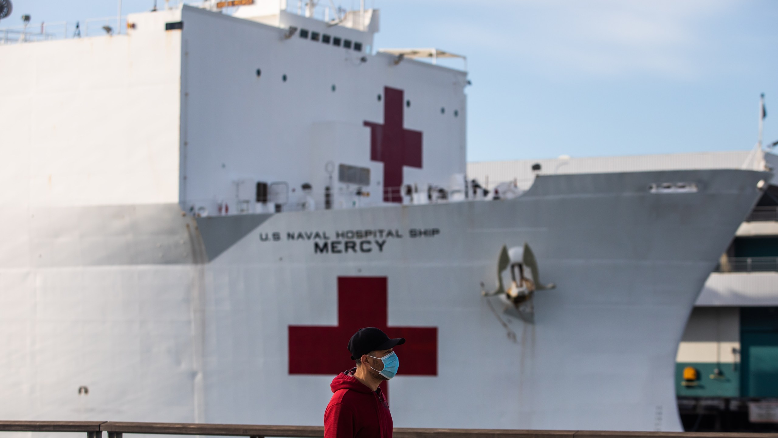 A man in a face mask walks past the U.S. Navy hospital ship, the USNS Mercy, on March 28, 2020, at the Port of Los Angeles in San Pedro. (Apu Gomes/AFP via Getty Images)