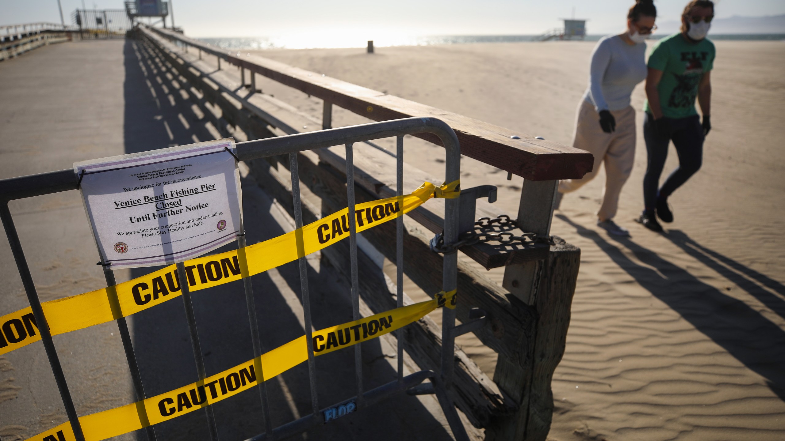 A barricade blocks the closed pier at Venice Beach as people walk past wearing face masks amid the coronavirus pandemic on March 27, 2020, in Venice, Calif. Los Angeles County closed all beaches that day as a measure to stem the spread of COVID-19. (Mario Tama/Getty Images)