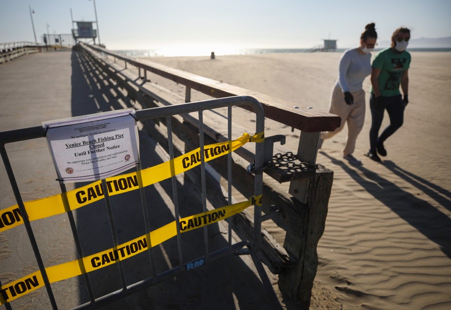 A barricade blocks the closed pier at Venice Beach as people walk past wearing face masks amid the coronavirus pandemic on March 27, 2020, in Venice, Calif. Los Angeles County closed all beaches that day as a measure to stem the spread of COVID-19. (Mario Tama/Getty Images)