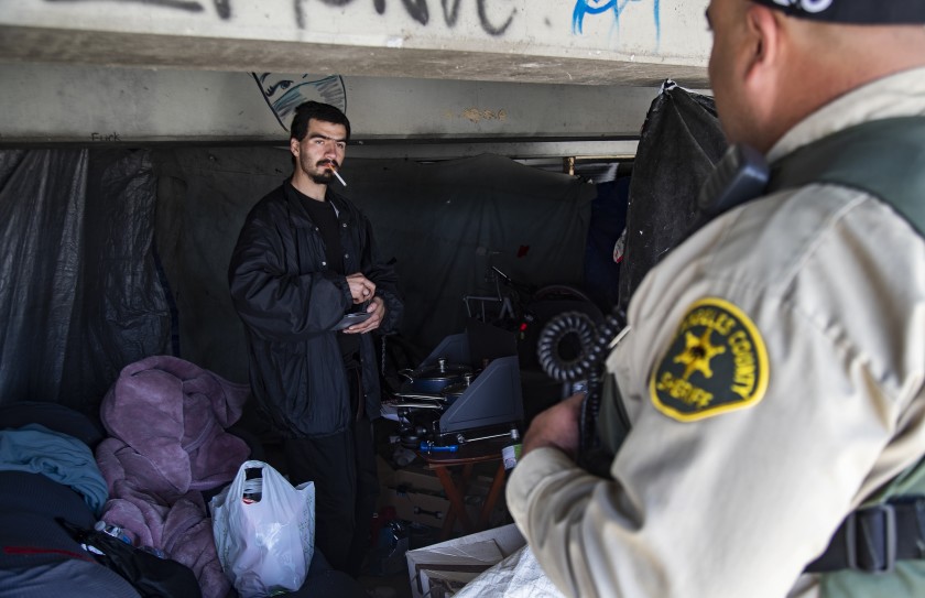 L.A. County Sheriff Deputy Michael Tadrous talks with Shawn Troncozo, 24, about how to prevent becoming infected with the novel coronavirus during an outreach effort in El Monte in March, 2020. (Gina Ferazzi/Los Angeles Times)