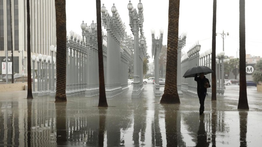 A visitor to the Los Angeles County Museum of Art makes his way through the rain and walks by Chris Burden’s sculpture “Urban Light” during an atmospheric river storm in February 2019. The first atmospheric river of 2020 will make its way to L.A. next week.(Genaro Molina / Los Angeles Times)