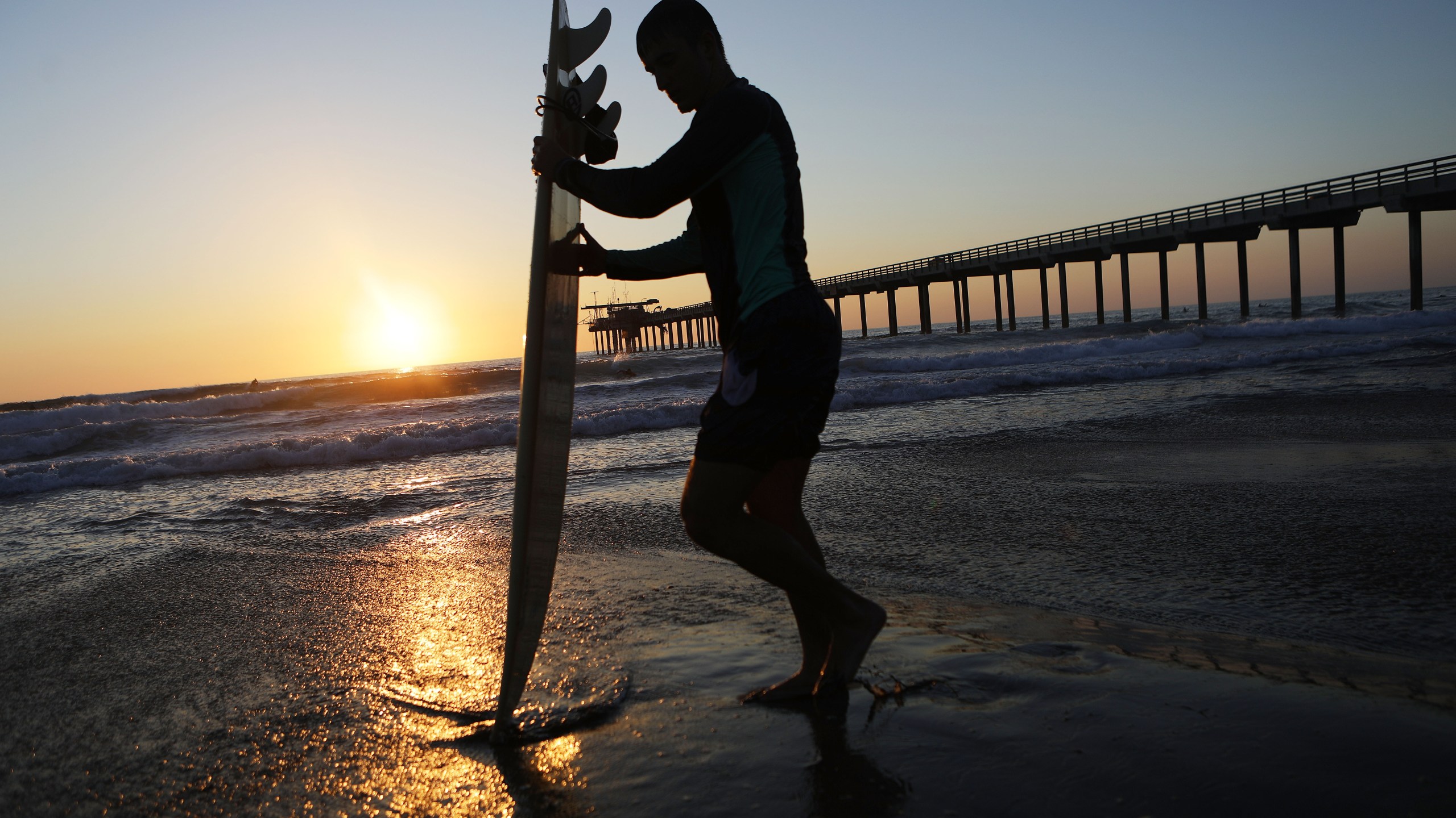 A surfer stands in front of Scripps Pier on the Pacific Ocean on August 7, 2018 in San Diego, California. (Mario Tama/Getty Images)