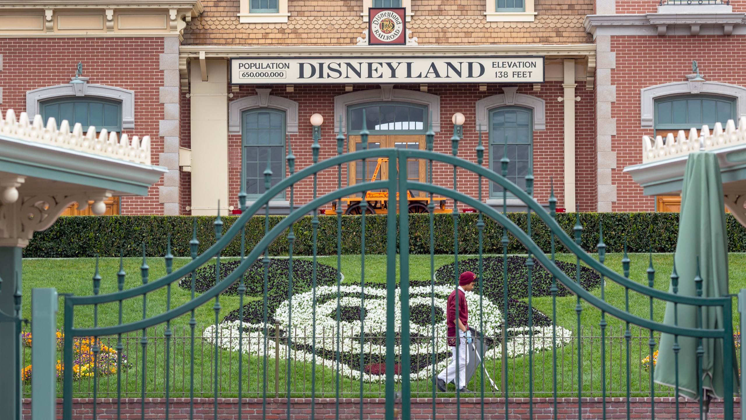 An employee cleans the grounds behind the closed gates of Disneyland Park on the first day of the closure of Disneyland and Disney California Adventure theme parks as fear of the spread of coronavirus continue, in Anaheim on March 14, 2020. (DAVID MCNEW/AFP via Getty Images)