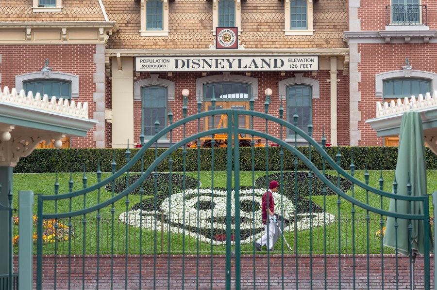 An employee cleans the grounds behind the closed gates of Disneyland in Anaheim on the first day of the resort’s closure amid fear of the spread of coronavirus, March 14, 2020. (David McNew / AFP / Getty Images)