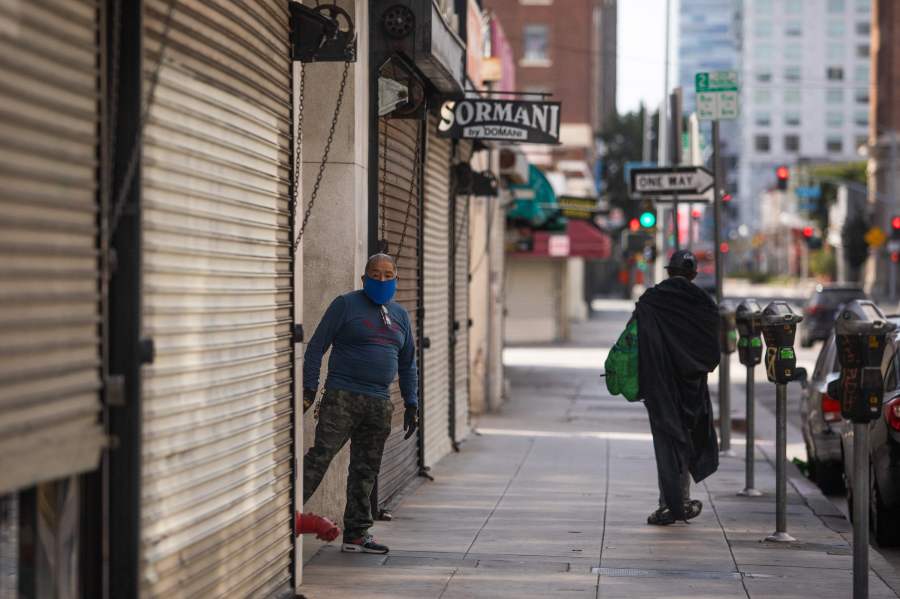 A private security guard wearing a face mask stands next to closed stores in the Fashion District in Downtown Los Angeles on April 2, 2020.(Apu Gomes/AFP via Getty Images)