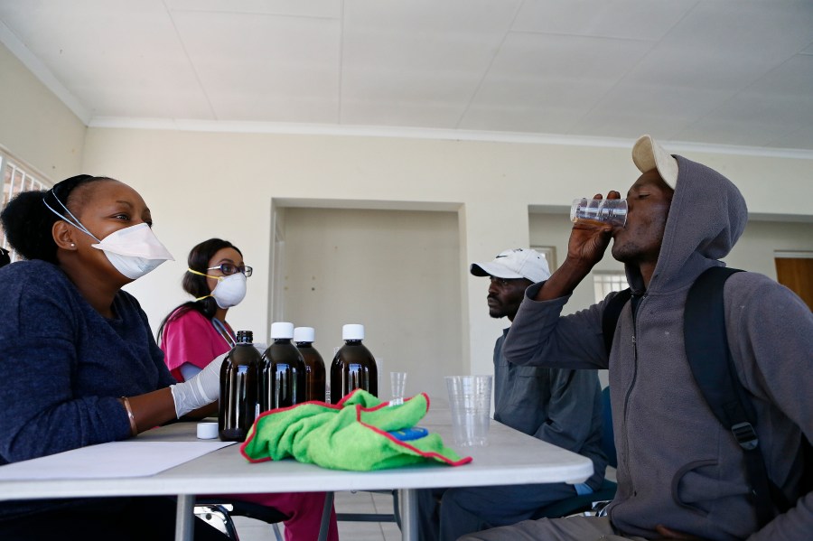 Health professionals look on as a homeless man drinks the Methadone Oral Solution, provided as an effort to care for drug-dependent people, at a shelter at the Lyttelton Sports Centre in Pretoria on April 16, 2020. The building is a temporary shelter being provided for homeless people amid the COVID-19 pandemic in South Africa. (Phill Magakoe / AFP via Getty Images)