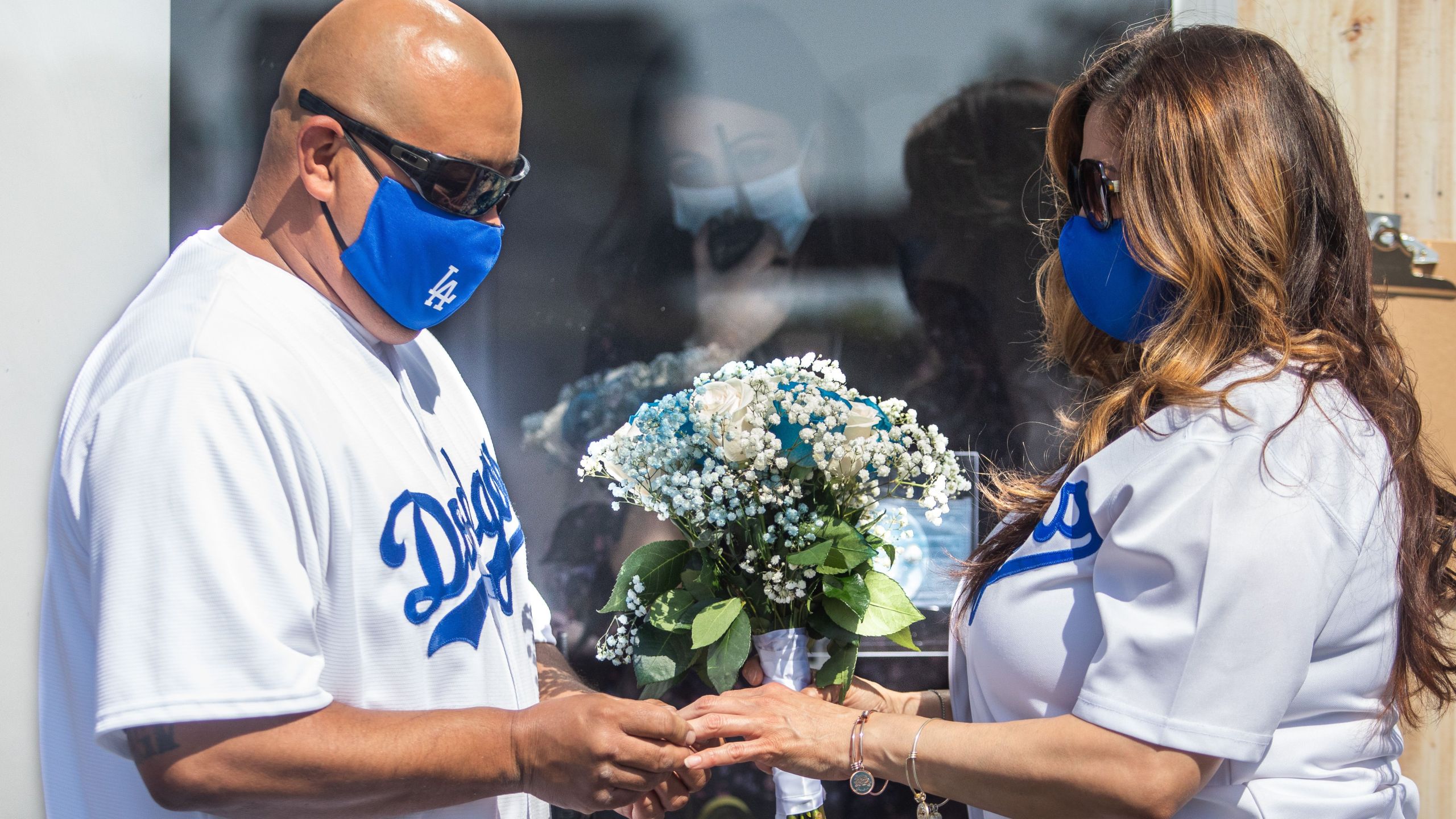 Philip Hernandez (L) puts the ring on his bride Marcela Peru, as Clerk Recorder Erika Patronas (C) looks on, during their wedding ceremony on April 21, 2020 in Anaheim, California. - The County of Orange Clerk Recorder employees implemented a variety of social distancing techniques to safely issue licenses and marry couples during the novel coronavirus pandemic. (APU GOMES/AFP via Getty Images)