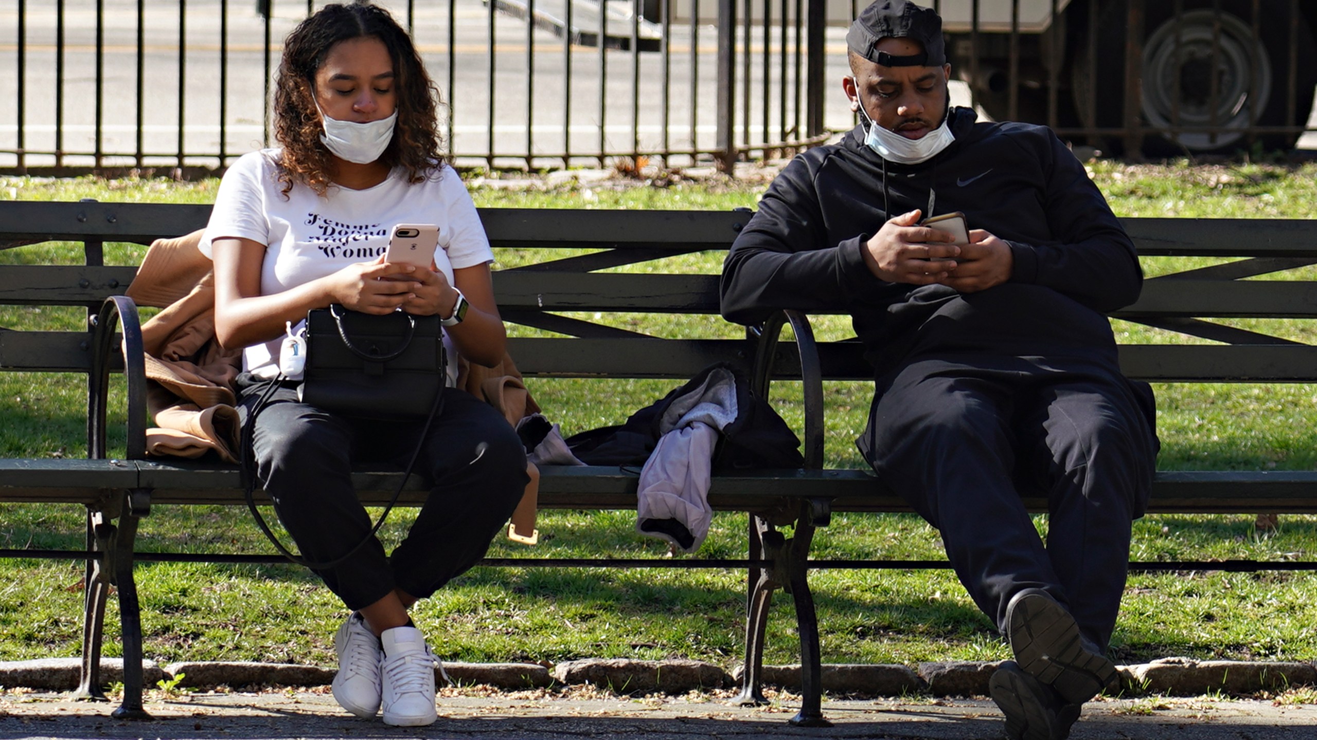 Two people sitting on a bench wearing protective masks use their phones on March 27, 2020, in New York City. (Cindy Ord/Getty Images)