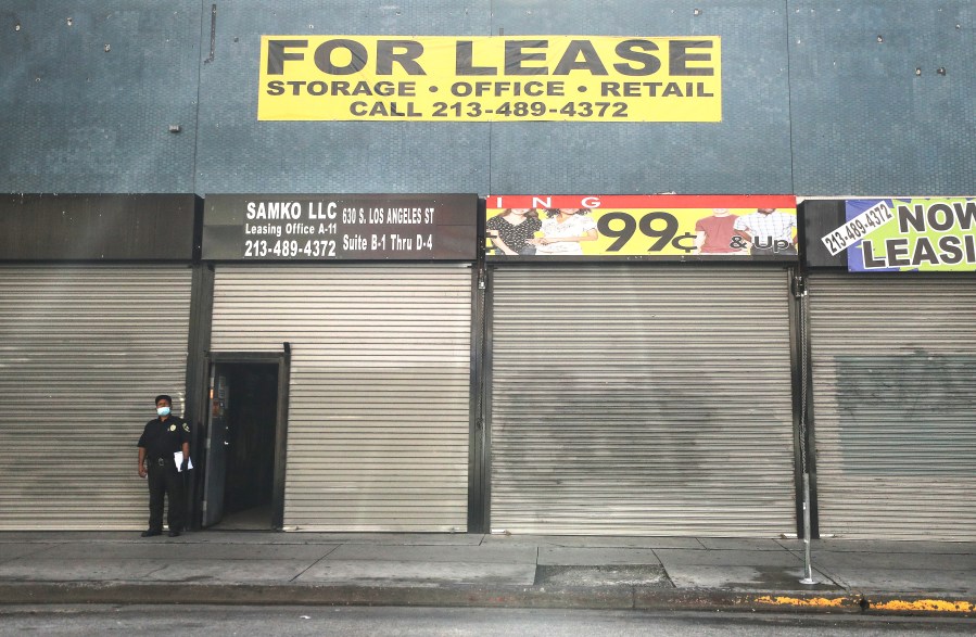 A security guard wears a face mask while standing outside shuttered shops and a 'For Lease' sign amid the global coronavirus pandemic on March 30, 2020 in Los Angeles, California. (Mario Tama/Getty Images)