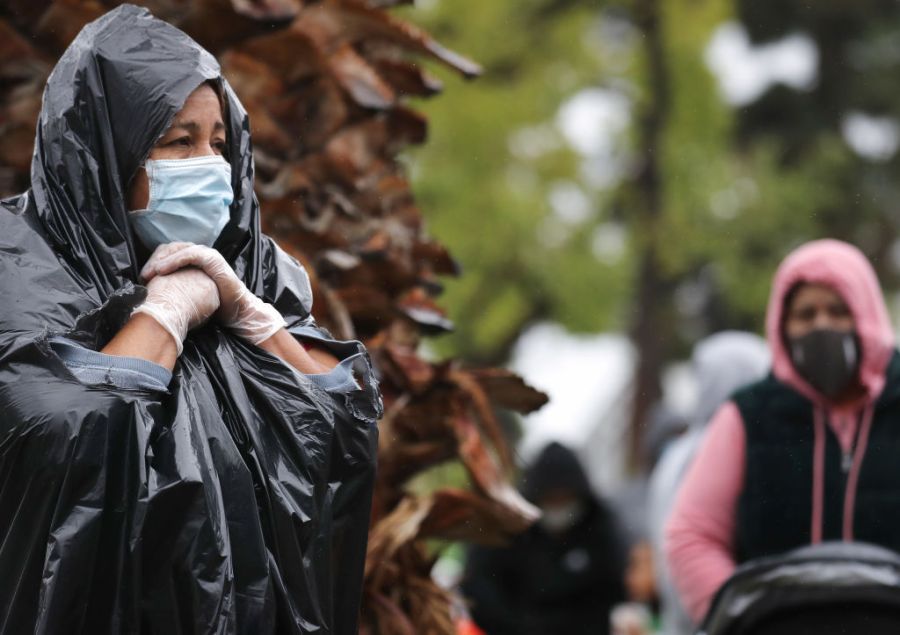 Juana Gomez, 50, from North Hollywood, wears a face mask and gloves, while using a trash bag to protect against the rain, as she waits in line to receive food at a Food Bank distribution for those in need as the coronavirus pandemic continues on April 9, 2020, in Van Nuys, California. (Mario Tama/Getty Images)