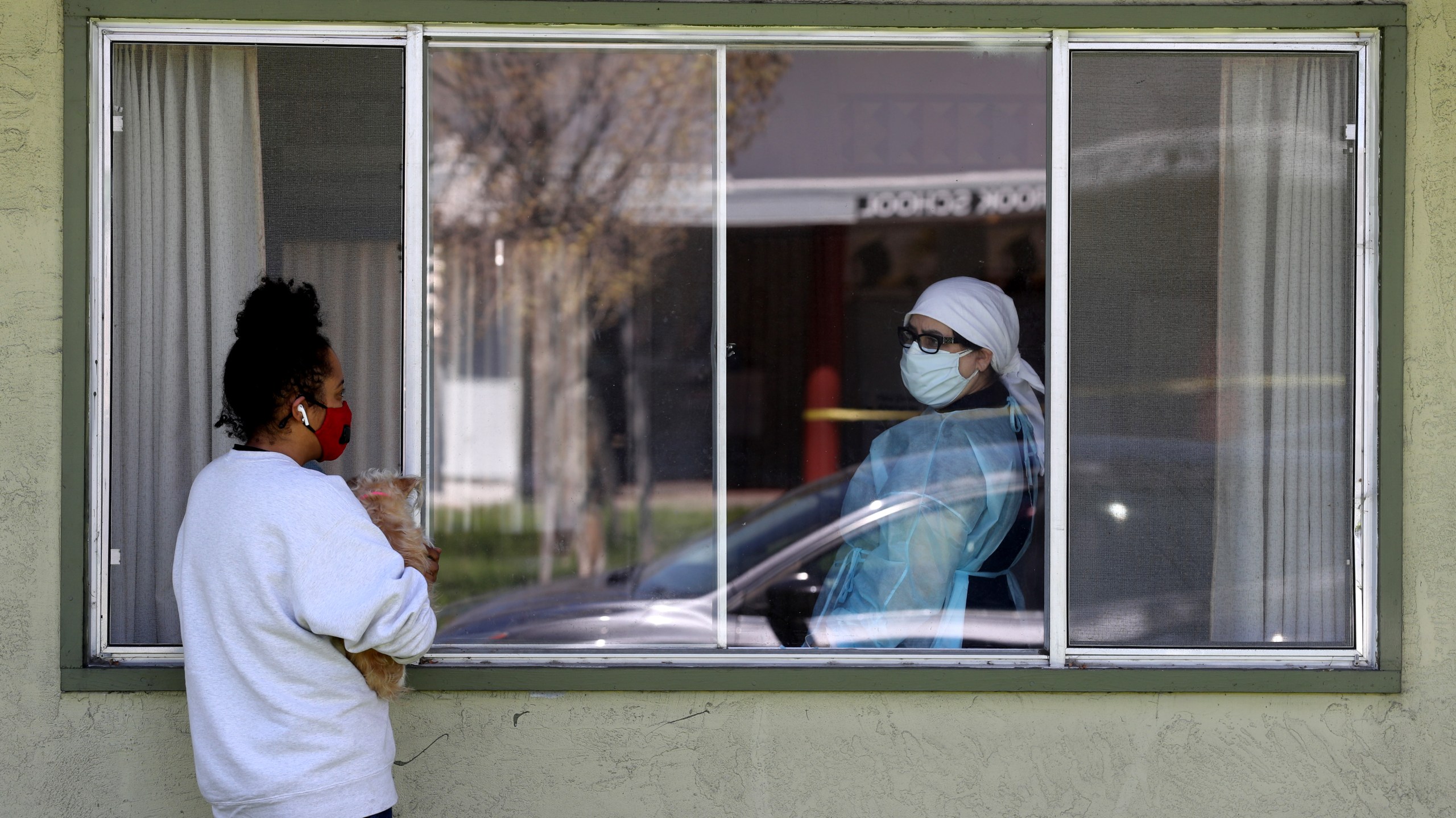 A woman talks with a nurse through a window as she visits her father who is a patient at a nursing home with a cluster of COVID-19 cases in Hayward, California, on April 14, 2020. (Justin Sullivan/Getty Images)