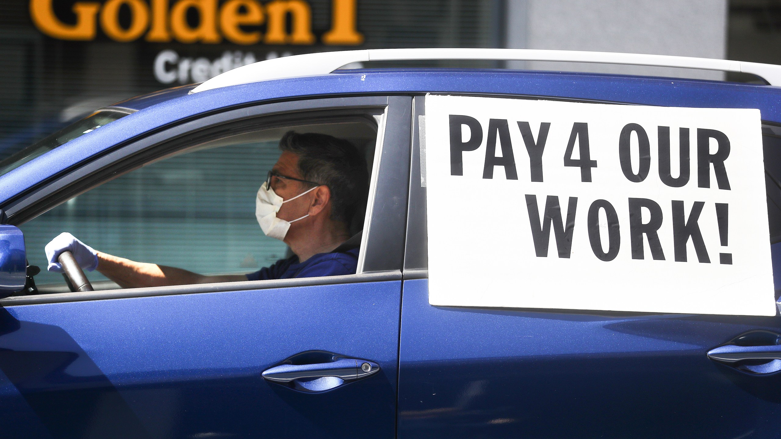 A driver wears a face mask and gloves as Uber and Lyft drivers with Rideshare Drivers United and the  Transport Workers Union of America conduct a" "caravan protest" outside the California Labor Commissioner’s office amidst the coronavirus pandemic on April 16, 2020 in Los Angeles. (Mario Tama/Getty Images)