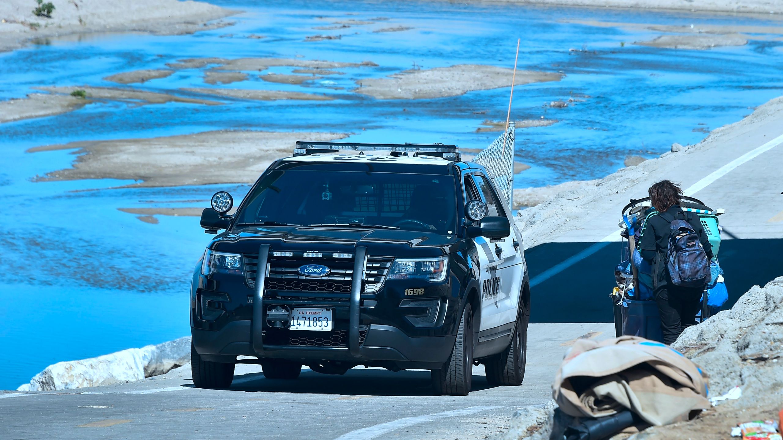 An officer from the Sheriff's Department speaks with a homless woman pulling her cart of belongings beside the Santa Ana River in Anaheim on February 20, 2018. (FREDERIC J. BROWN/AFP via Getty Images)