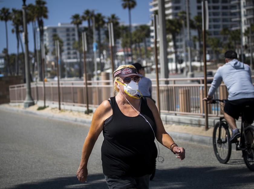 A woman wears a protective mask while exercising on the boardwalk in Huntington Beach on April 2, 2020. (Credit: Allen J. Schaben / Los Angeles Times)