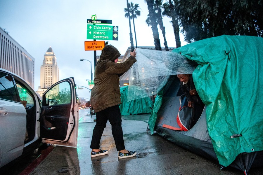 Melissa Acedera distributes meals and supplies to one of her contacts, Harvey, on Olvera Street on a rainy evening in downtown Los Angeles. The COVID-19 pandemic and ensuing hoarding have disrupted food supply lines to shelters and organizations that feed L.A.'s homeless residents.(Mariah Tauger / Los Angeles Times)