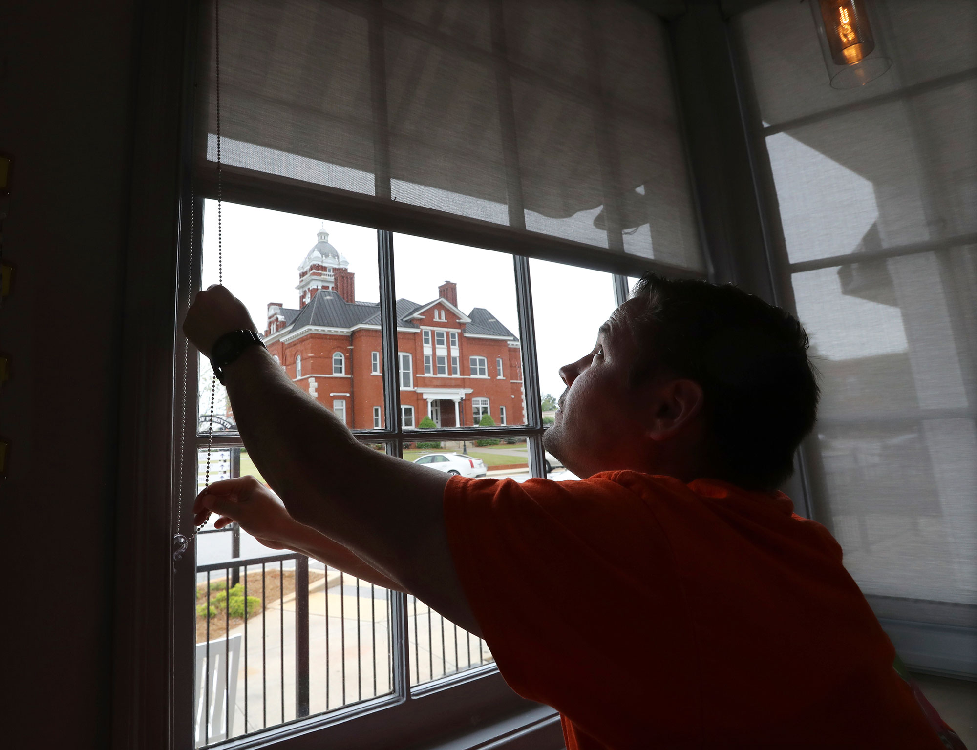 Brian Lambert, owner of a coffee and sweets shop in Forsyth, Georgia, opens the windows of his business as he gets ready to reopen next week. (Curtis Compton/AP via CNN Wire)