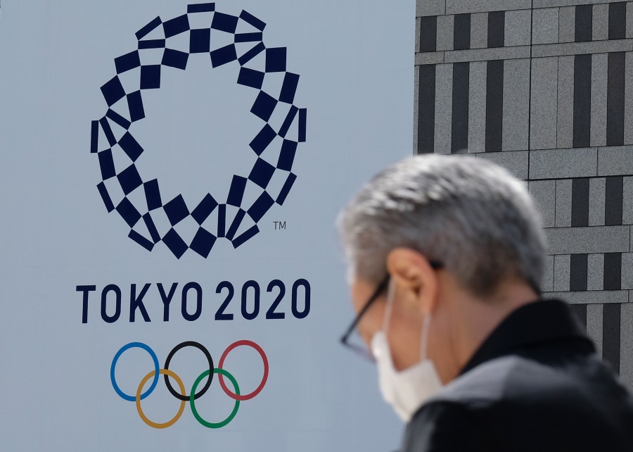 A man wearing a face mask walks before the logo of the Tokyo 2020 Olympic Games displayed on the Tokyo Metropolitan Government building in Tokyo on March 24, 2020. - The International Olympic Committee came under pressure to speed up its decision about postponing the Tokyo Games on March 24 as athletes criticised the four-week deadline and the United States joined calls to delay the competition. (Photo by Kazuhiro NOGI / AFP) (Photo by KAZUHIRO NOGI/AFP via Getty Images)