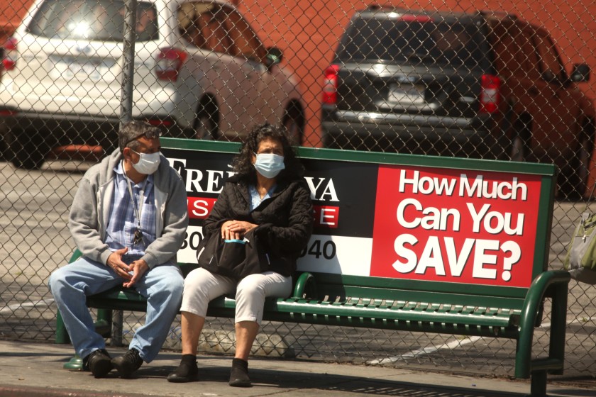 A man and a woman wear masks while waiting for a bus in Los Angeles in this undated photo. (Genaro Molina / Los Angeles Times)